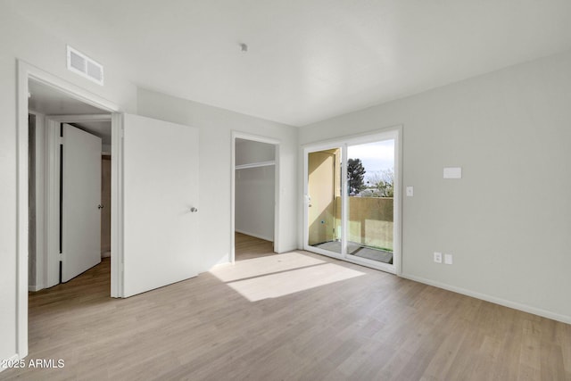 unfurnished bedroom featuring access to exterior, visible vents, a walk in closet, and wood finished floors