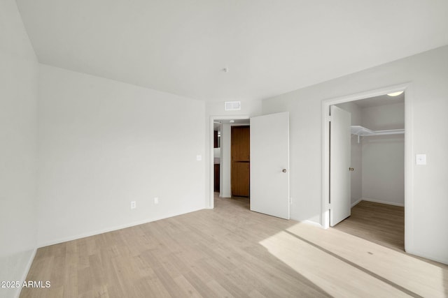 unfurnished bedroom with visible vents, a walk in closet, baseboards, light wood-type flooring, and a closet