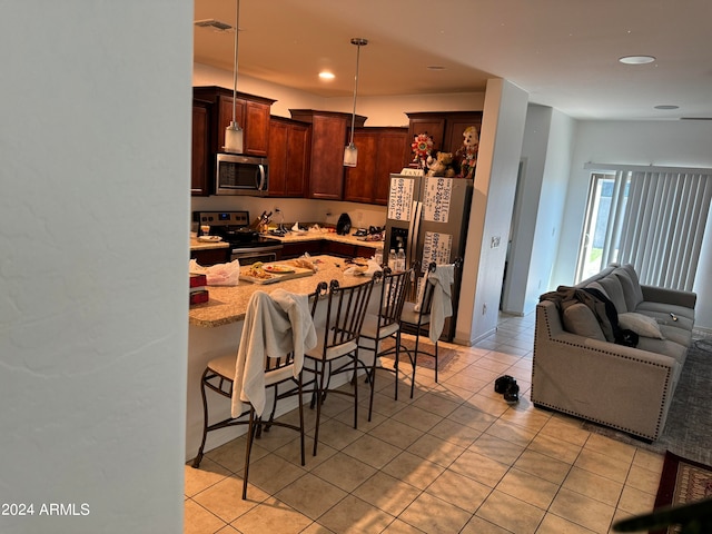 kitchen with appliances with stainless steel finishes, light tile floors, decorative light fixtures, a kitchen breakfast bar, and light stone countertops