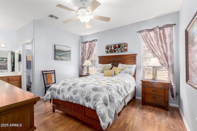 bedroom featuring multiple windows, light wood-type flooring, ceiling fan, and connected bathroom