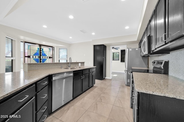 kitchen featuring appliances with stainless steel finishes, sink, backsplash, ceiling fan, and light stone counters