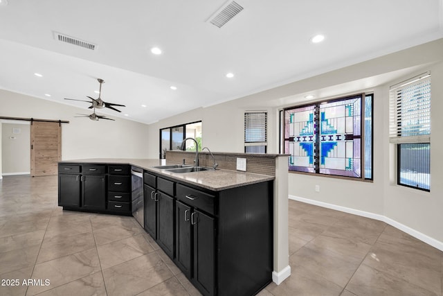 kitchen featuring sink, light stone countertops, a barn door, a center island with sink, and lofted ceiling