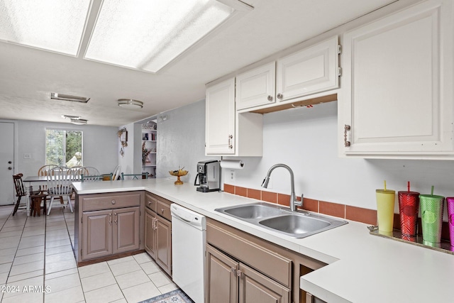 kitchen with kitchen peninsula, white dishwasher, light tile floors, sink, and white cabinetry