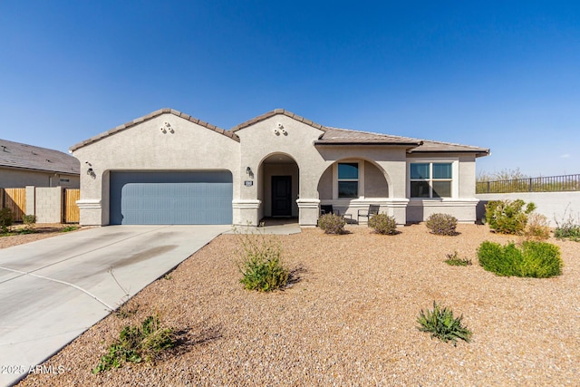 mediterranean / spanish home featuring a tile roof, stucco siding, concrete driveway, fence, and a garage