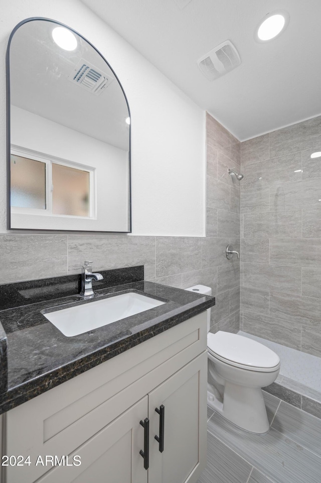 bathroom featuring toilet, vanity, tile walls, tile patterned floors, and tiled shower