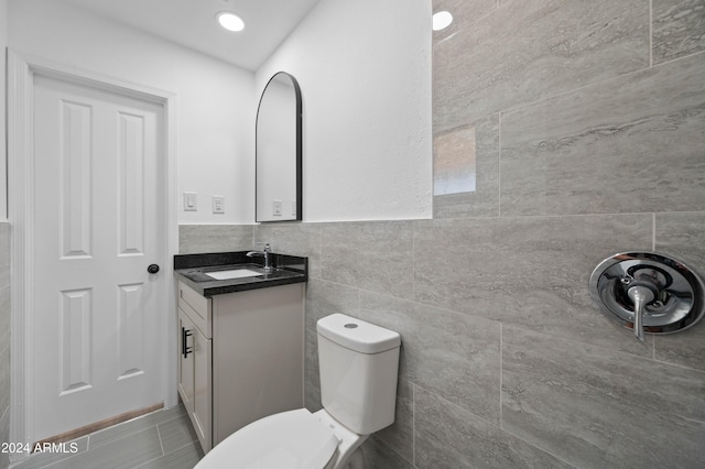 bathroom with tile patterned floors, toilet, vanity, and tile walls