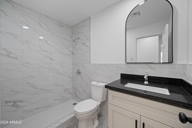 bathroom with toilet, vanity, tile walls, and a tile shower