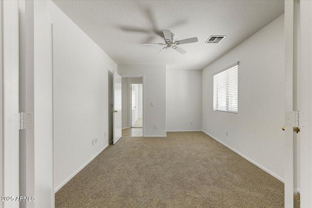 empty room with ceiling fan, visible vents, light carpet, and baseboards