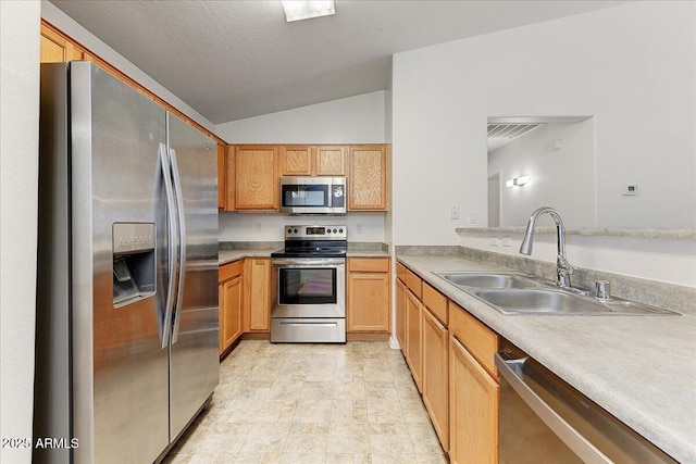 kitchen with stone finish floor, light countertops, a sink, appliances with stainless steel finishes, and vaulted ceiling