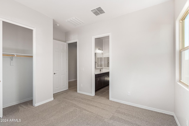 unfurnished bedroom featuring a closet, light colored carpet, sink, and connected bathroom