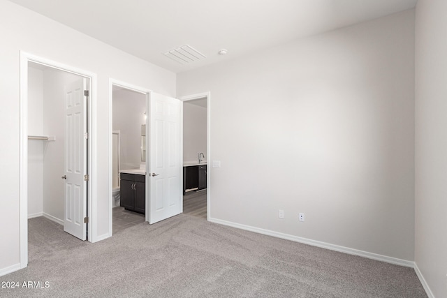 unfurnished bedroom featuring light colored carpet, connected bathroom, a closet, and a spacious closet