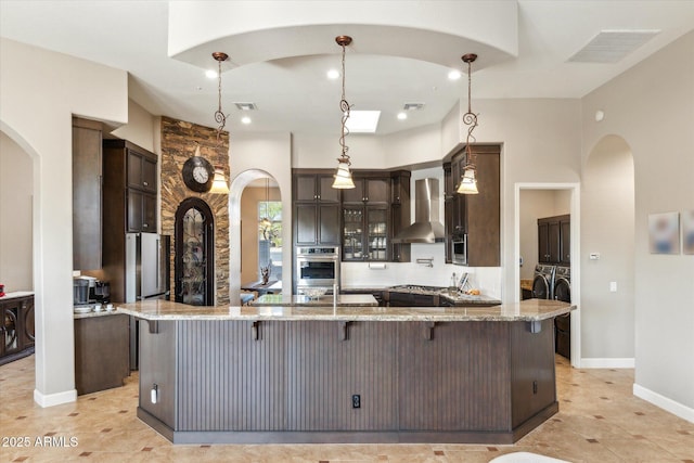 34096 N 87th Way, Scottsdale, AZ 85266 - kitchen featuring washing machine and clothes dryer, visible vents, arched walkways, a kitchen bar, and wall chimney exhaust hood