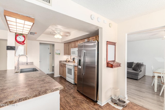 kitchen with white appliances, a ceiling fan, visible vents, a sink, and a raised ceiling