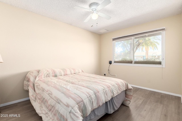 bedroom with a ceiling fan, wood finished floors, baseboards, and a textured ceiling