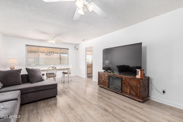 living area featuring baseboards, ceiling fan, a textured ceiling, and light wood-style floors