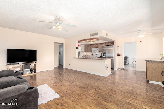 living room with a textured ceiling, wood finished floors, visible vents, and ceiling fan