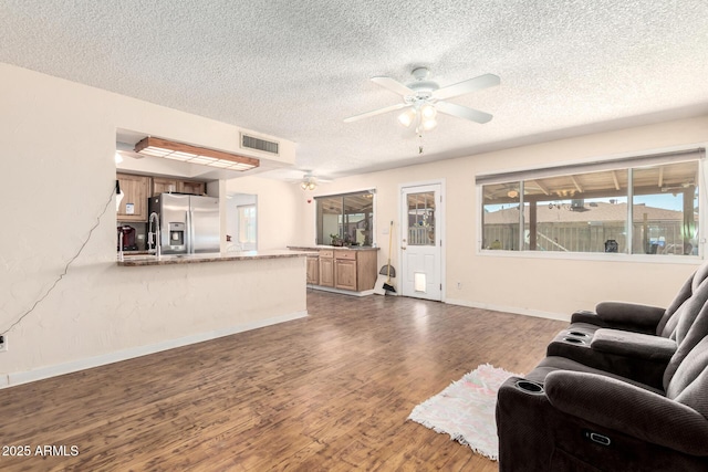 living area featuring visible vents, a ceiling fan, a textured ceiling, wood finished floors, and baseboards