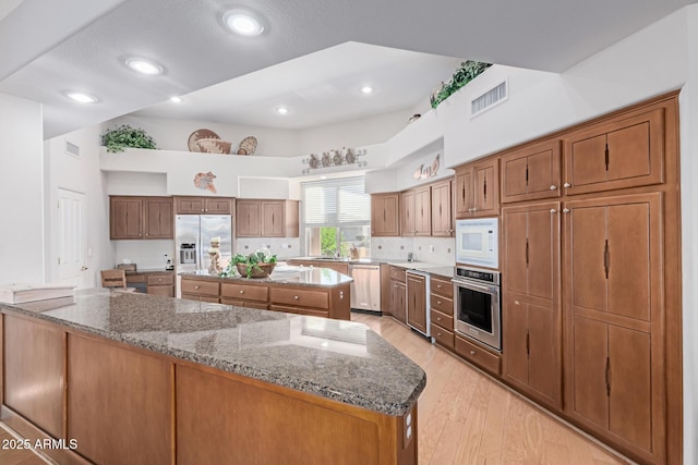 24801 N Vado Ct, Rio Verde, AZ 85263 - kitchen featuring stainless steel appliances, light stone countertops, a center island, light wood-type flooring, and backsplash