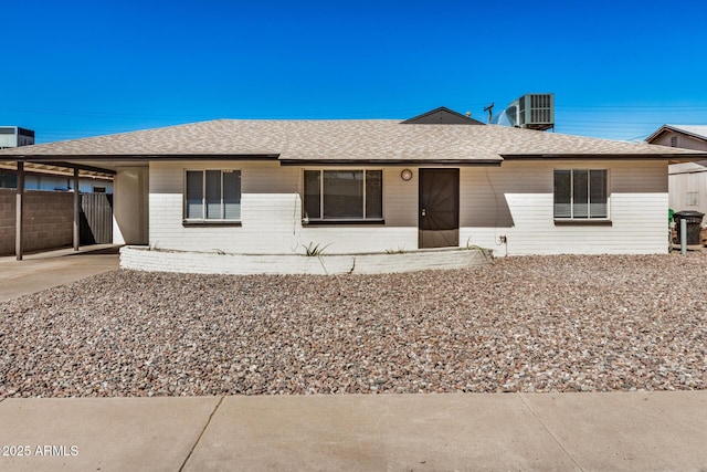 ranch-style house with central air condition unit, fence, a shingled roof, an attached carport, and brick siding