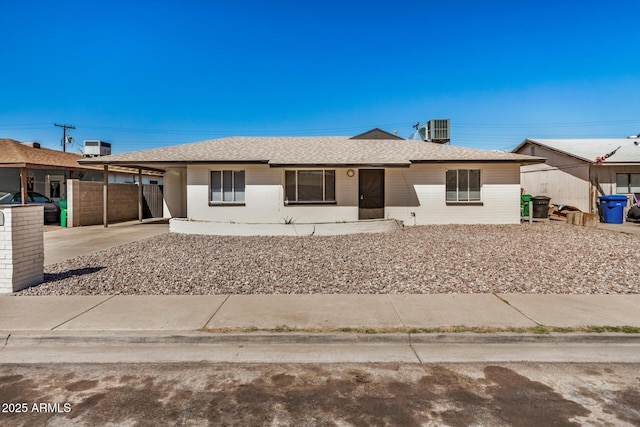 ranch-style home featuring a carport, central AC unit, concrete driveway, and a shingled roof