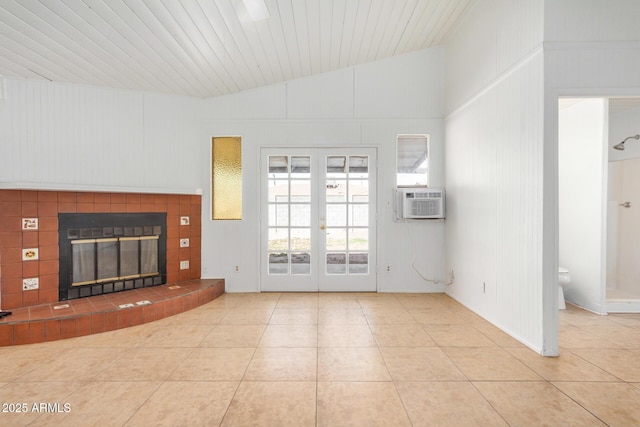 unfurnished living room featuring cooling unit, vaulted ceiling, french doors, a tiled fireplace, and tile patterned floors