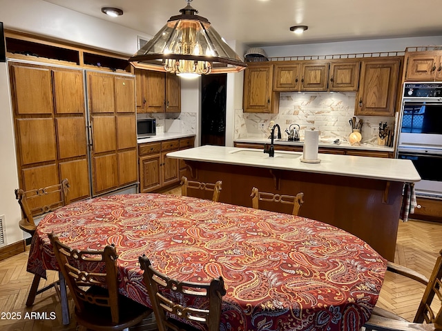 kitchen featuring pendant lighting, light parquet floors, backsplash, and an island with sink