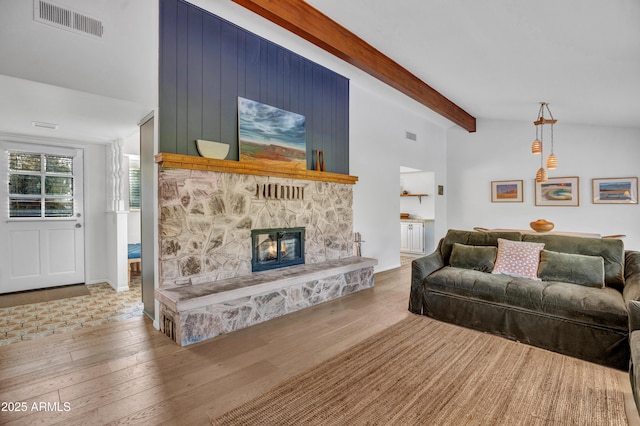 living room with beamed ceiling, visible vents, a stone fireplace, and wood finished floors