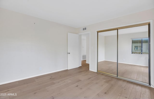 unfurnished bedroom featuring baseboards, visible vents, wood finished floors, and a closet