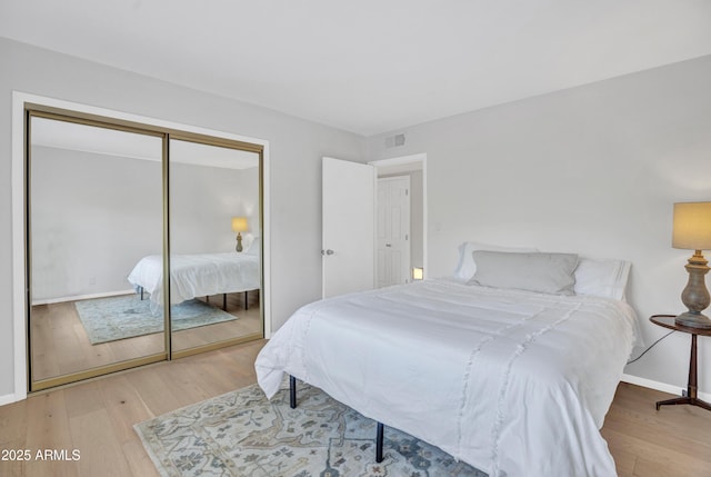 bedroom featuring baseboards, visible vents, wood finished floors, and a closet