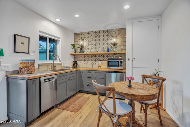 kitchen with a sink, decorative backsplash, gray cabinets, wooden counters, and appliances with stainless steel finishes