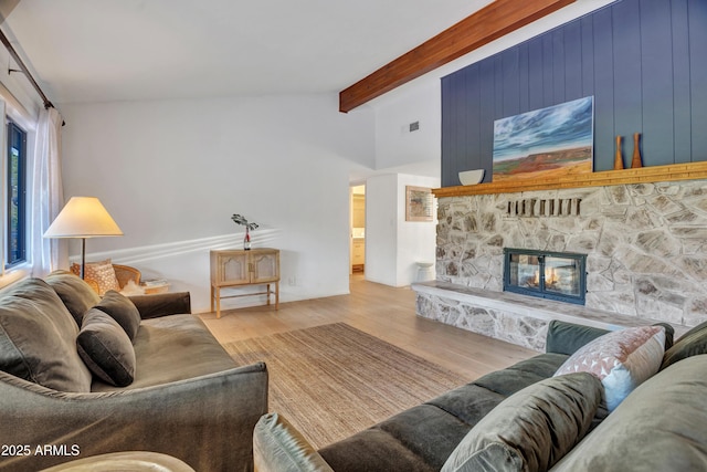 living area with a stone fireplace, vaulted ceiling with beams, wood finished floors, and visible vents