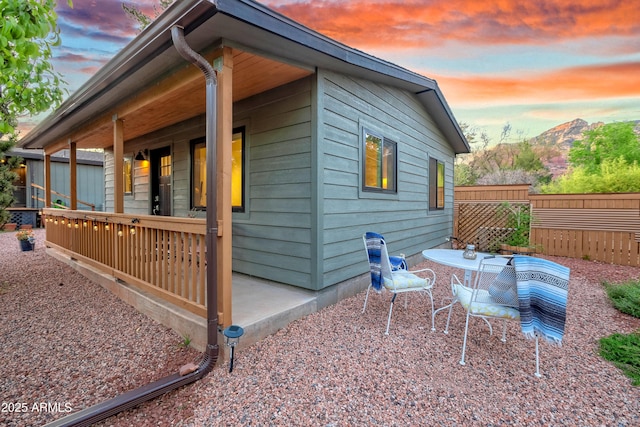 property exterior at dusk with covered porch, a mountain view, and fence