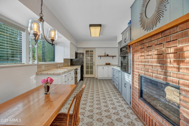 kitchen featuring white cabinetry, open shelves, a sink, tile counters, and black appliances