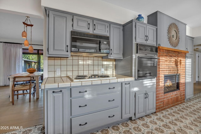 kitchen featuring black appliances, decorative backsplash, gray cabinets, and tile countertops