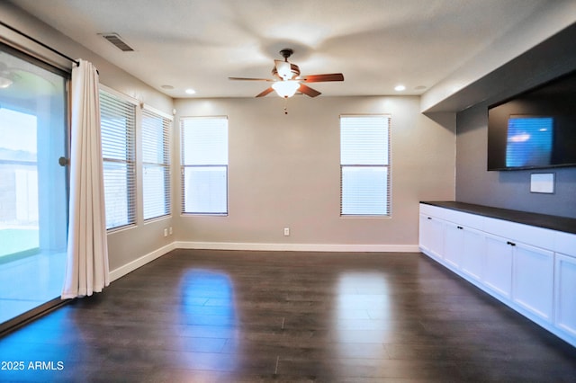 unfurnished living room with dark wood-type flooring, a ceiling fan, visible vents, and baseboards