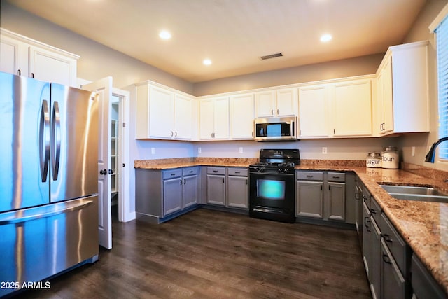 kitchen with dark wood-style floors, gray cabinets, appliances with stainless steel finishes, a sink, and light stone countertops