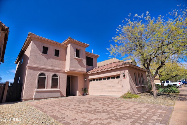 mediterranean / spanish house with a garage, a tiled roof, decorative driveway, and stucco siding