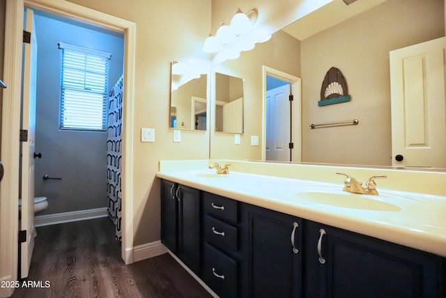 full bathroom featuring double vanity, baseboards, toilet, wood finished floors, and a sink