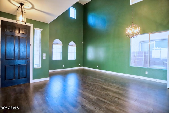 entrance foyer with dark wood-style floors, a high ceiling, an inviting chandelier, and baseboards