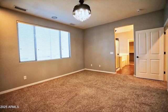 carpeted empty room with baseboards, visible vents, and a chandelier