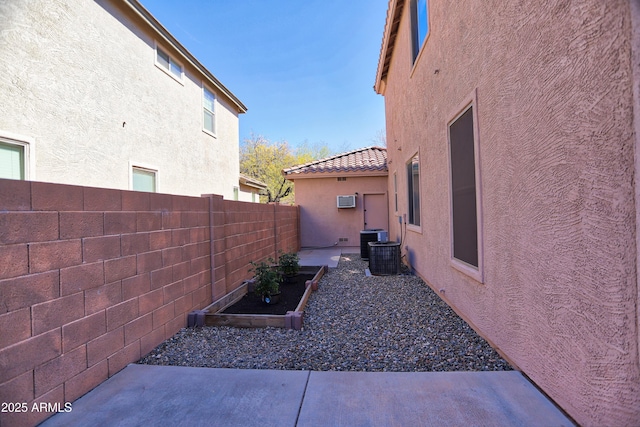 view of home's exterior with a wall mounted AC, a fenced backyard, a garden, and stucco siding