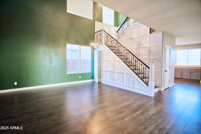 unfurnished living room featuring dark wood-type flooring, a chandelier, stairway, and baseboards