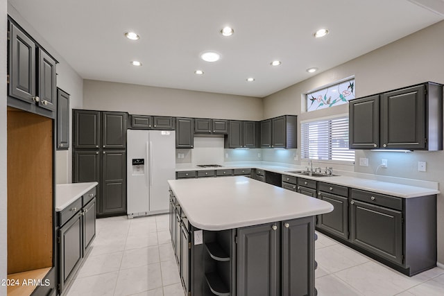 kitchen with gray cabinetry, white refrigerator with ice dispenser, a kitchen island, light tile patterned floors, and sink