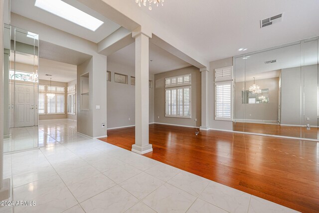 unfurnished room featuring an inviting chandelier, light wood-type flooring, and decorative columns