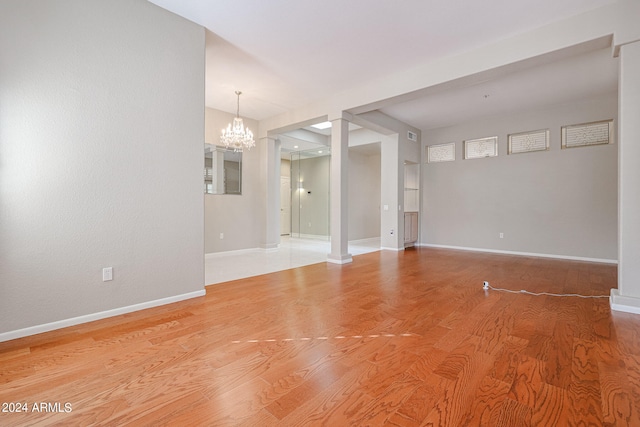 empty room featuring wood-type flooring, an inviting chandelier, and ornate columns