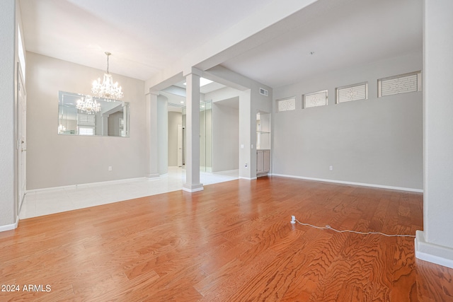 unfurnished living room with an inviting chandelier, hardwood / wood-style flooring, and ornate columns