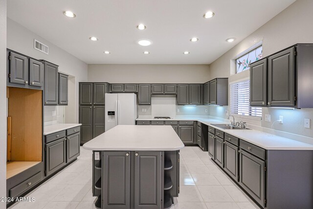 kitchen with white refrigerator with ice dispenser, light tile patterned floors, gray cabinets, a center island, and gas cooktop