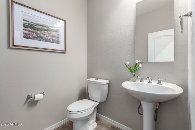 half bath with baseboards, toilet, wood finished floors, and a textured wall