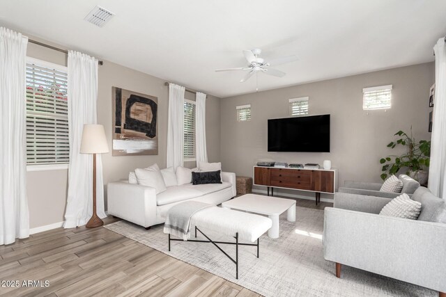 living area with a wealth of natural light, visible vents, ceiling fan, and wood finished floors