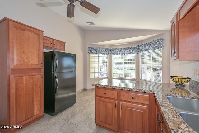 kitchen with kitchen peninsula, black fridge, light stone counters, vaulted ceiling, and ceiling fan